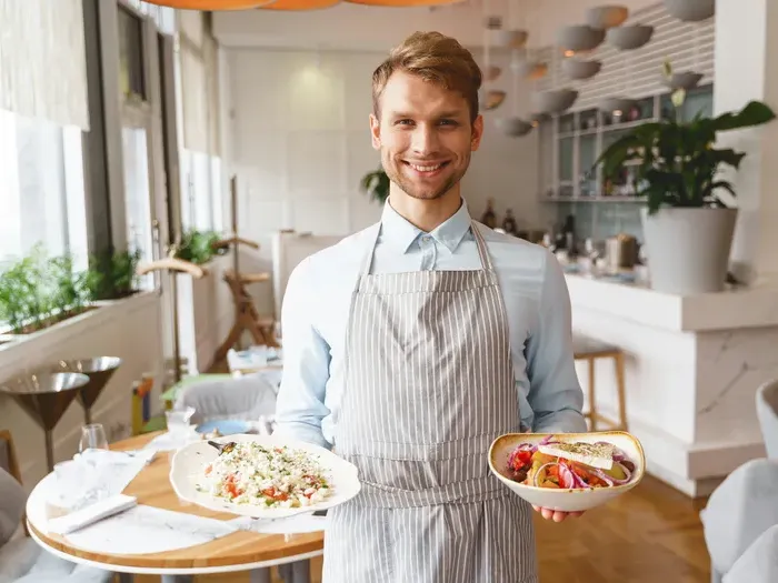 Restaurant server in apron presenting two colorful dishes inside a bright cafe, representing local eateries